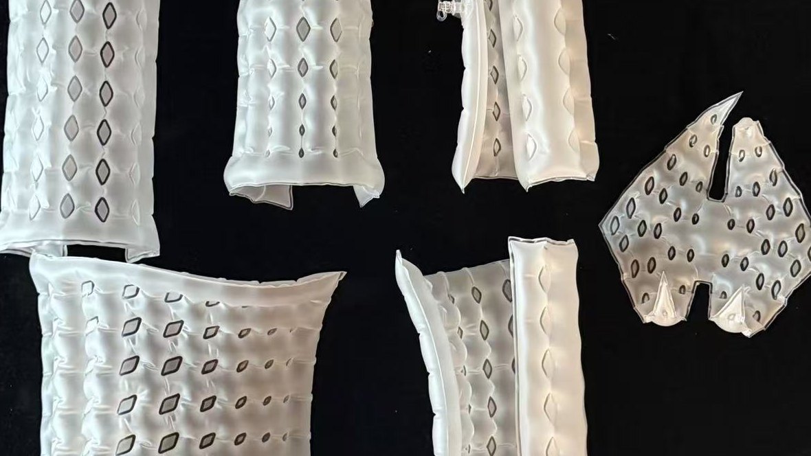Six heat-sealed TPU inflatable sheet prototypes with diamond seam patterns, curling and bending on a black board