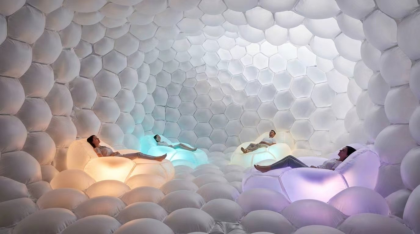 People resting in glowing inflatable seats inside a soft cellular inflatable enclosure